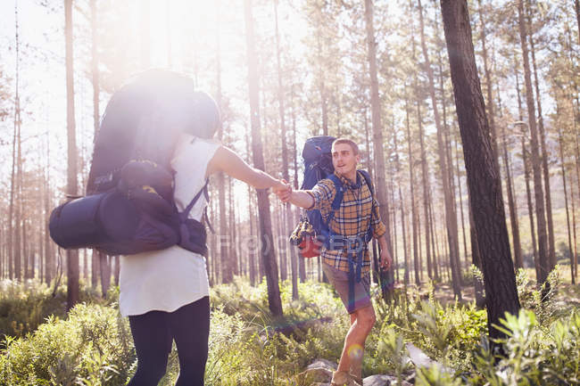 Young man helping girlfriend on hiking trail in sunny woods — Stock Photo