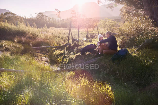 Coppia giovane con zaini trekking, riposo in soleggiato campo remoto — Foto stock