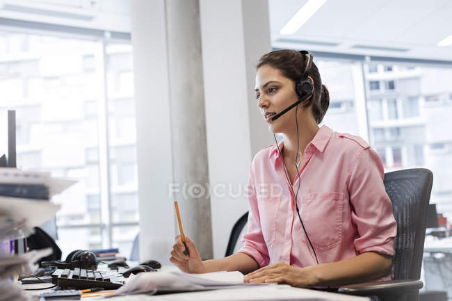 Mujer de negocios con dispositivo manos libres hablando por teléfono en el escritorio de la oficina - foto de stock