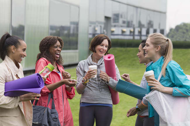 Mulheres amigas com tapetes de ioga e café conversando fora do ginásio — Fotografia de Stock
