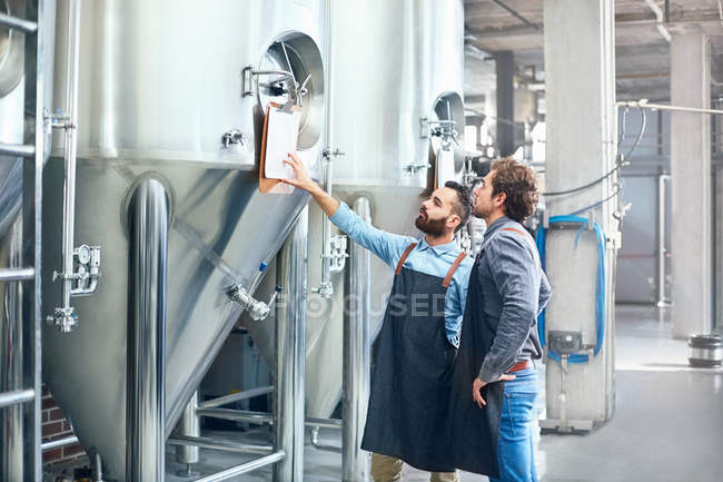 Male brewers checking clipboard on vat — Stock Photo