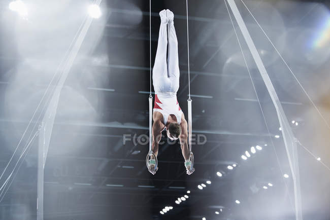 Male gymnast balancing upside down on gymnastics rings in arena — Stock Photo