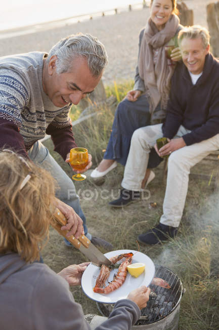 Couples d'âge mûr barbecue et boire du vin sur la plage — Photo de stock
