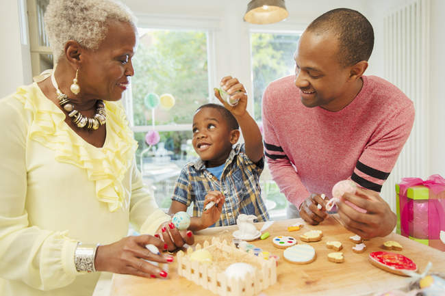 Семья из нескольких поколений украшает пасхальные яйца и печенье на кухне — стоковое фото