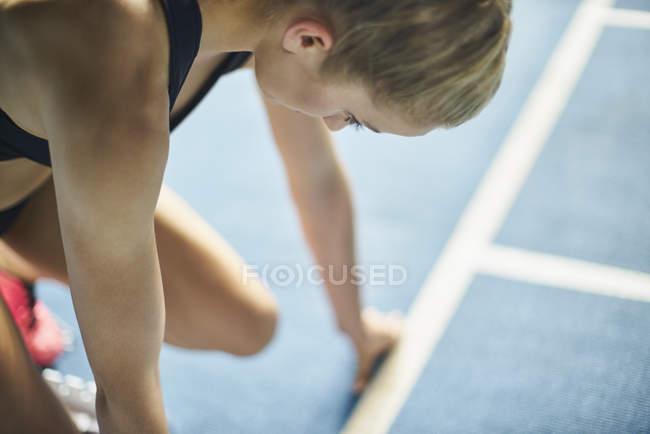 Corredor femenino enfocado listo en el bloque de partida en pista deportiva - foto de stock