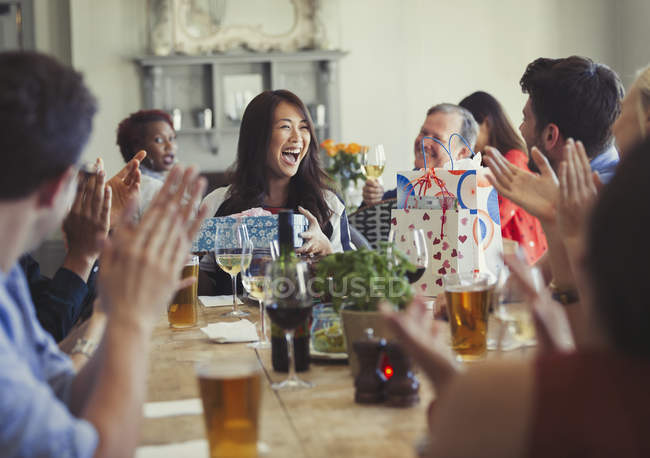 Amigos aplaudiendo por mujer feliz celebrando cumpleaños en la mesa del restaurante - foto de stock