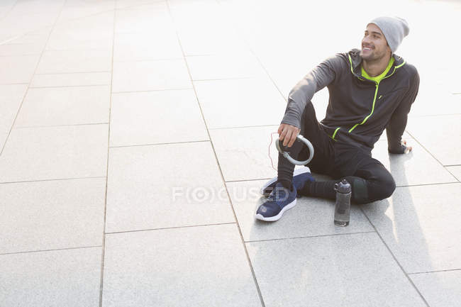 Lächelnder männlicher Läufer, der sich ausruht, Kopfhörer hält und wegschaut — Stockfoto