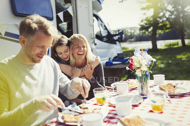 Feliz família abraçando e comendo café da manhã fora ensolarado motor casa — Fotografia de Stock