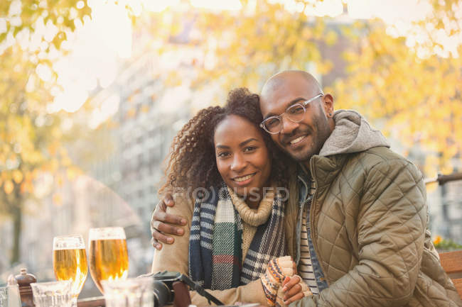 Portrait smiling young couple hugging and drinking beer at autumn sidewalk cafe — Stock Photo