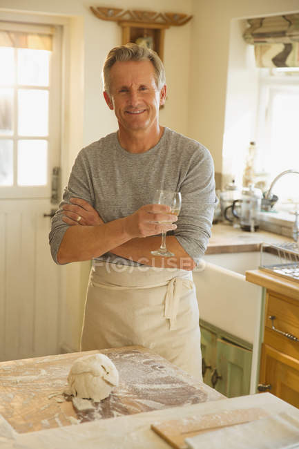 Портрет улыбающийся пожилой человек пьет вино и печет на кухне — стоковое фото