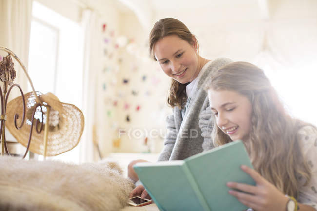 Two teenage girls reading book together on bed — Stock Photo