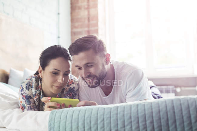 Paar benutzt Handy auf dem Bett — Stockfoto