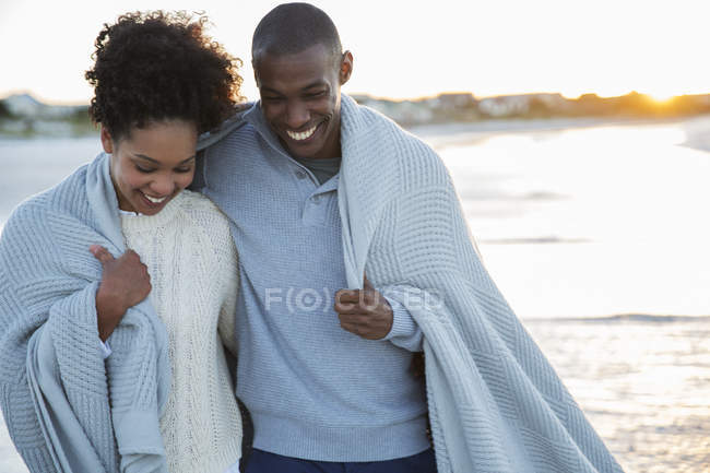 Portrait of couple wrapped in blanket on beach — Stock Photo