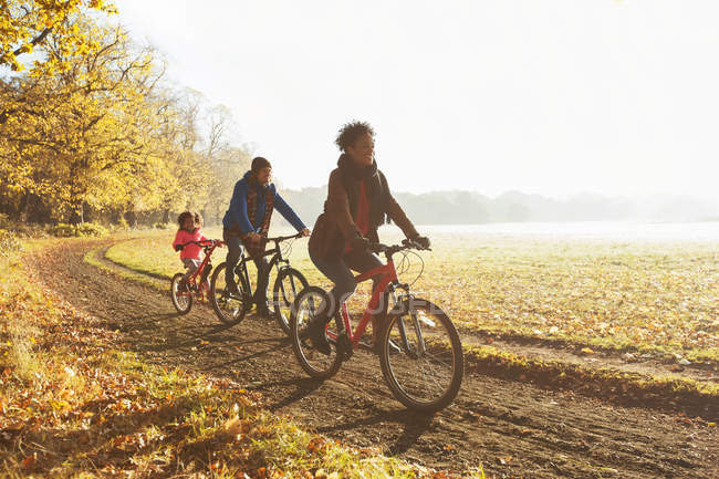 Giocoso giro in bici per famiglie lungo il sentiero nel soleggiato parco autunnale — Foto stock