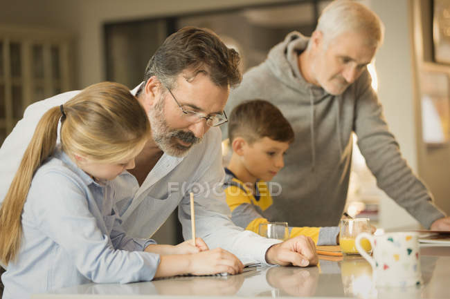 Male gay parents helping children doing homework at counter — Stock Photo