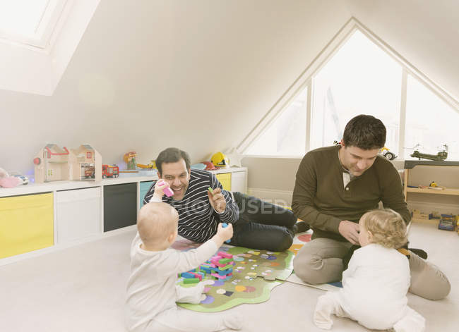 Родители-геи играют с маленькими сыновьями в игровой комнате — стоковое фото