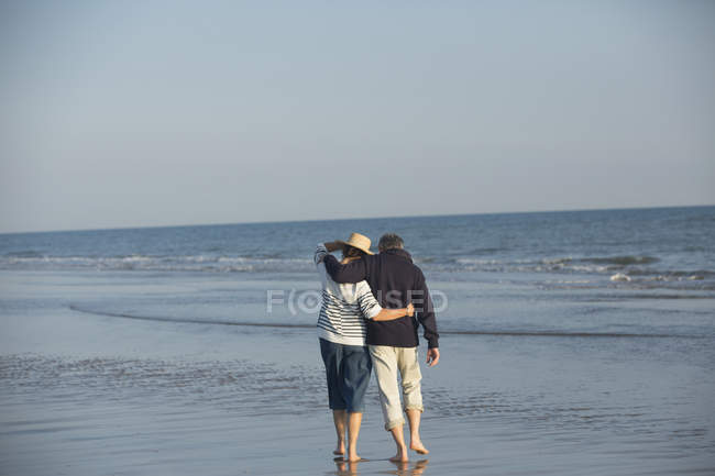 Affectionate mature couple hugging, walking in sunny ocean beach surf — Stock Photo