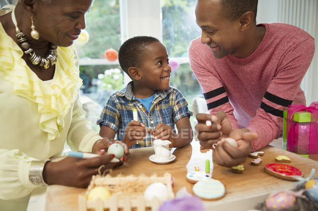 Familia multigeneracional que decora huevos y galletas de Pascua - foto de stock