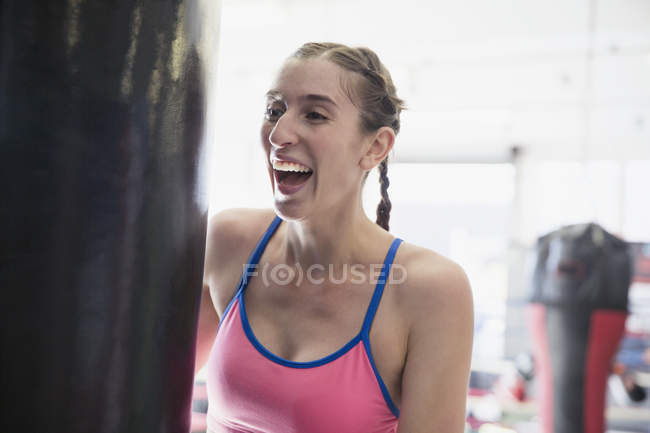 Rindo jovem boxeador do sexo feminino em saco de perfuração no ginásio — Fotografia de Stock