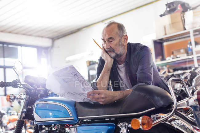 Focused senior meccanico motociclistico maschile revisione manuale in officina — Foto stock