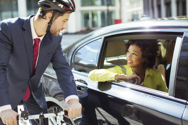 Businessman on bicycle talking to woman in car — Stock Photo