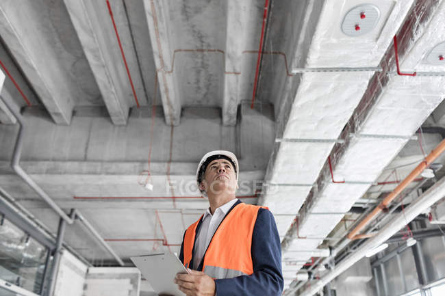 Foreman with clipboard looking up at construction site — Stock Photo