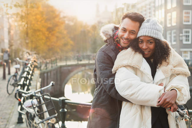 Portrait smiling young couple hugging in warm clothing along canal in Amsterdam — Stock Photo