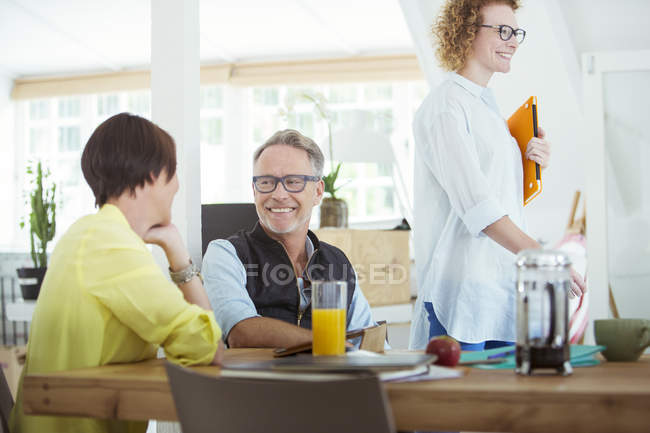 Улыбающиеся офисные работники разговаривают за столом во время перерыва — стоковое фото
