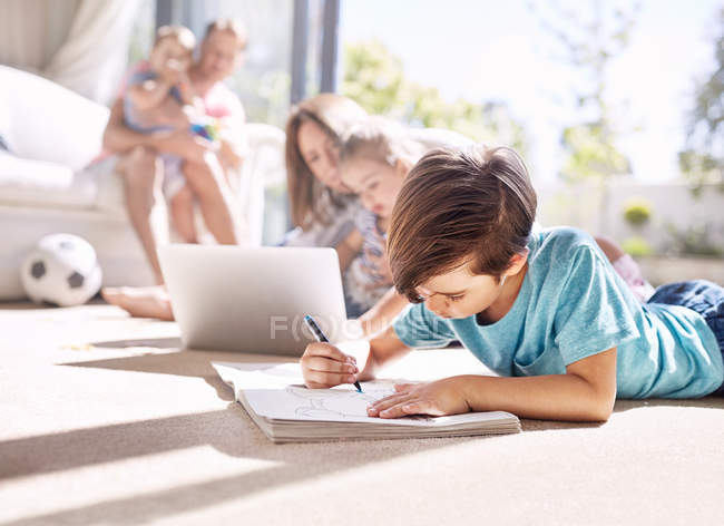Boy coloring in coloring book on sunny living room floor — Stock Photo