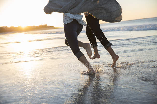 Pernas de jovem casal correndo na praia ao pôr do sol — Fotografia de Stock