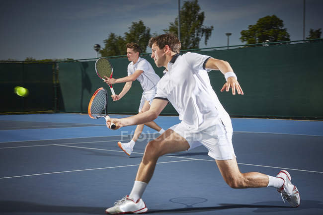Young male tennis doubles players playing tennis, hitting the ball on blue tennis court — Stock Photo
