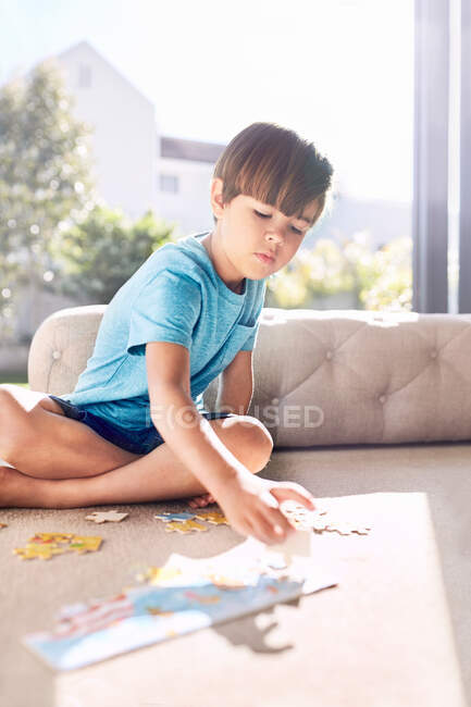 Сосредоточенный мальчик собирает пазл на диване — стоковое фото