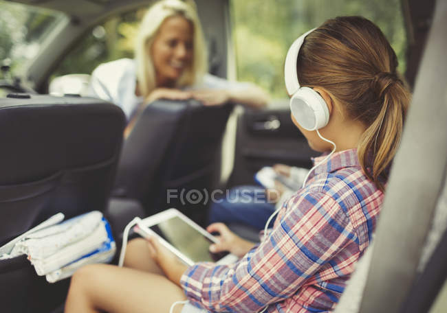Дівчина з навушниками за допомогою цифрового планшета дивиться відео на задньому сидінні автомобіля — стокове фото