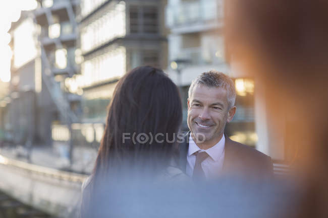 Улыбающийся бизнесмен слушает деловую женщину на городской улице — стоковое фото
