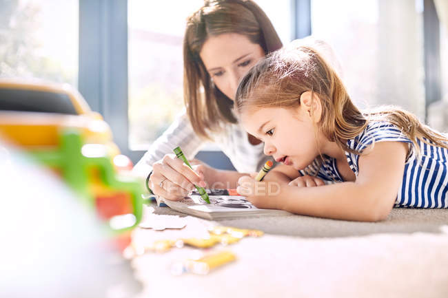 Mother and daughter coloring in coloring book with crayons — Stock Photo