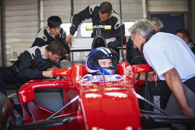 Manager parlando con pilota di Formula 1 auto da corsa in garage di riparazione — Foto stock