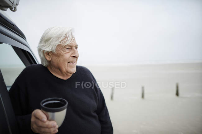 Heureux homme âgé boire du café en voiture sur la plage d'hiver — Photo de stock