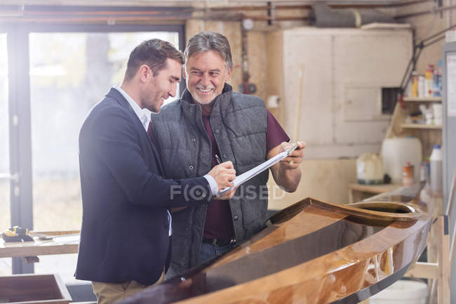 Male customer signing paperwork for finished wood kayak in workshop — Stock Photo