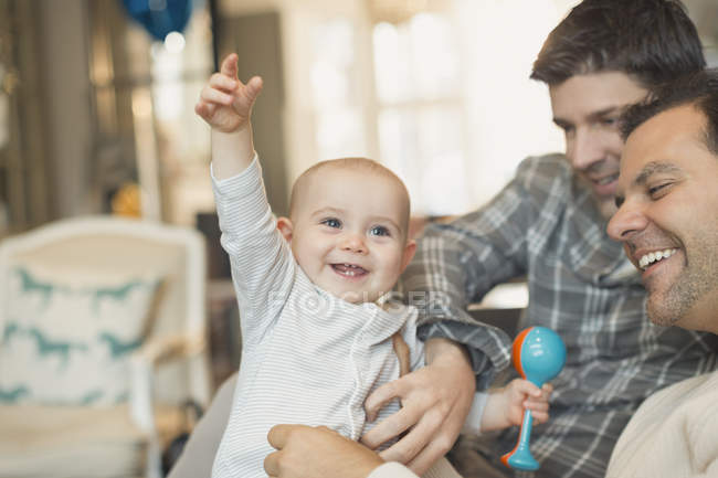 Playful, cute baby son with rattle and male gay parents — Stock Photo