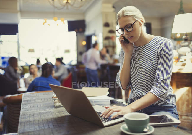 Empresária criativa falando no celular e usando laptop no café — Fotografia de Stock