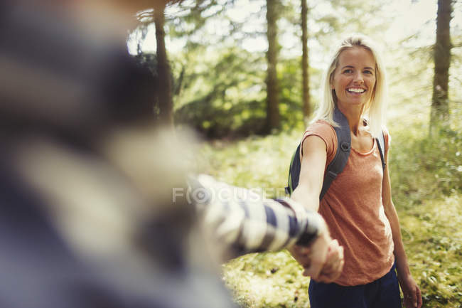 Sonriente pareja cogida de la mano senderismo en el bosque - foto de stock