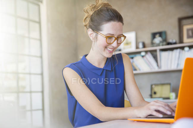 Портрет молодой женщины с оранжевым ноутбуком, работающей в домашнем офисе — стоковое фото