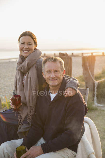 Портрет улыбающейся зрелой пары, пьющей вино на пляже на закате — стоковое фото