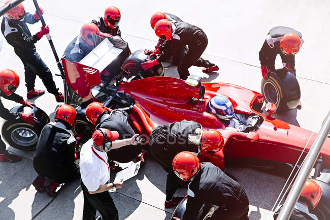 Manager with stopwatch timing pit crew replacing tires in pit lane — Stock Photo