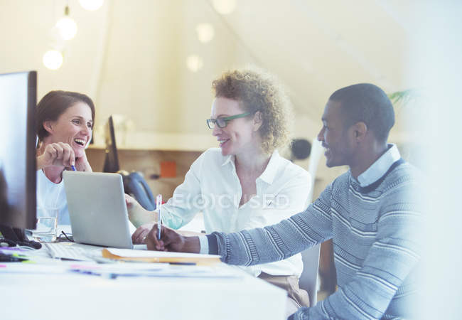 Office workers talking over laptop at desk — Stock Photo