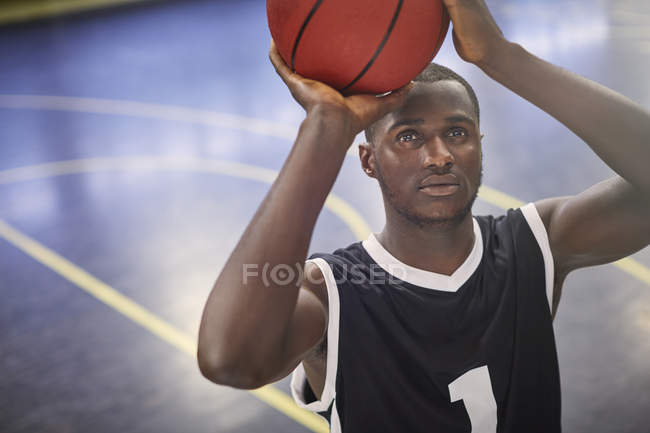 Enfocado joven jugador de baloncesto masculino disparando la pelota en la cancha - foto de stock