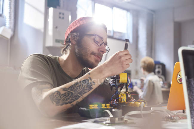 Сосредоточенный молодой дизайнер собирает робототехнику в мастерской — стоковое фото