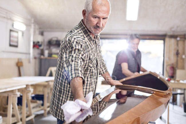Senior man finishing, wiping wood kayak in workshop — Stock Photo