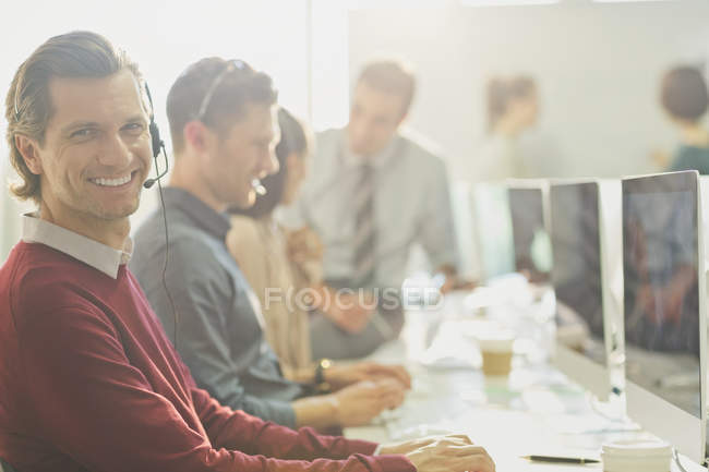 Портрет усміхненого телемаркетолога, що розмовляє по телефону з гарнітурою за комп'ютером — стокове фото