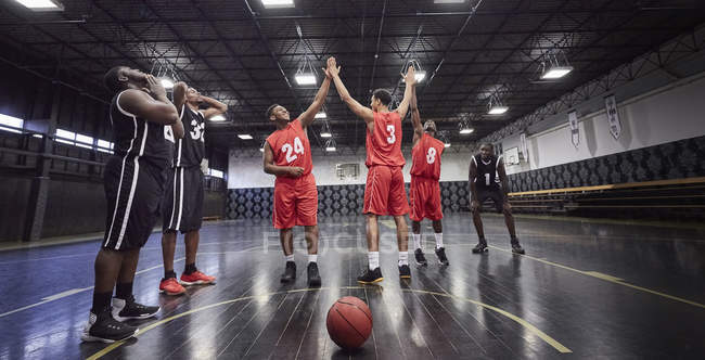 Jovens jogadores de basquete do sexo masculino high-fiving, comemorando na corte no ginásio — Fotografia de Stock